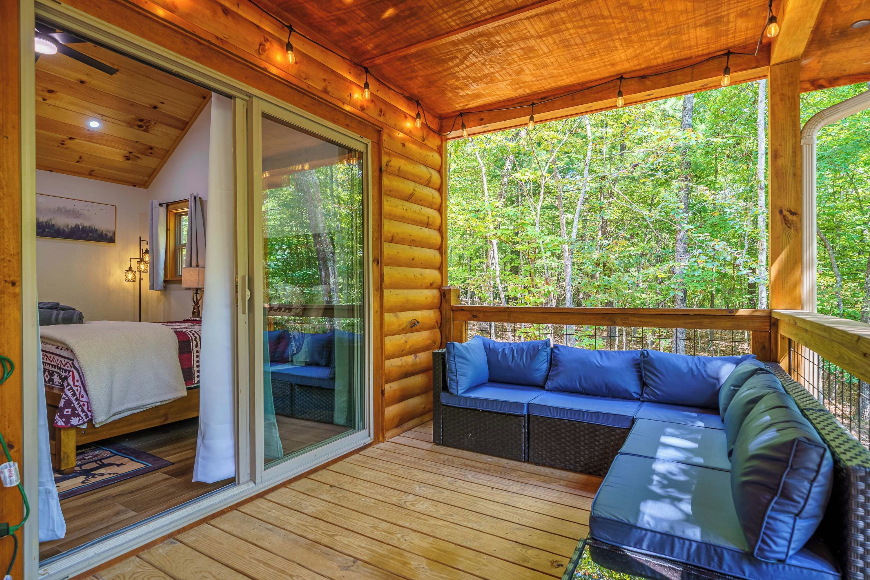 A log cabin with a bedroom, a living area with a sofa, and a glass door leading to a deck.