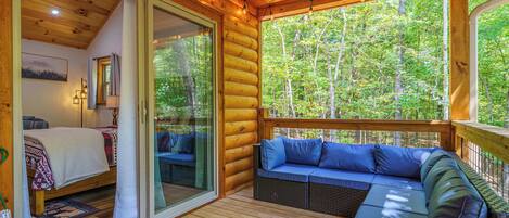 A log cabin with a bedroom, a living area with a sofa, and a glass door leading to a deck.