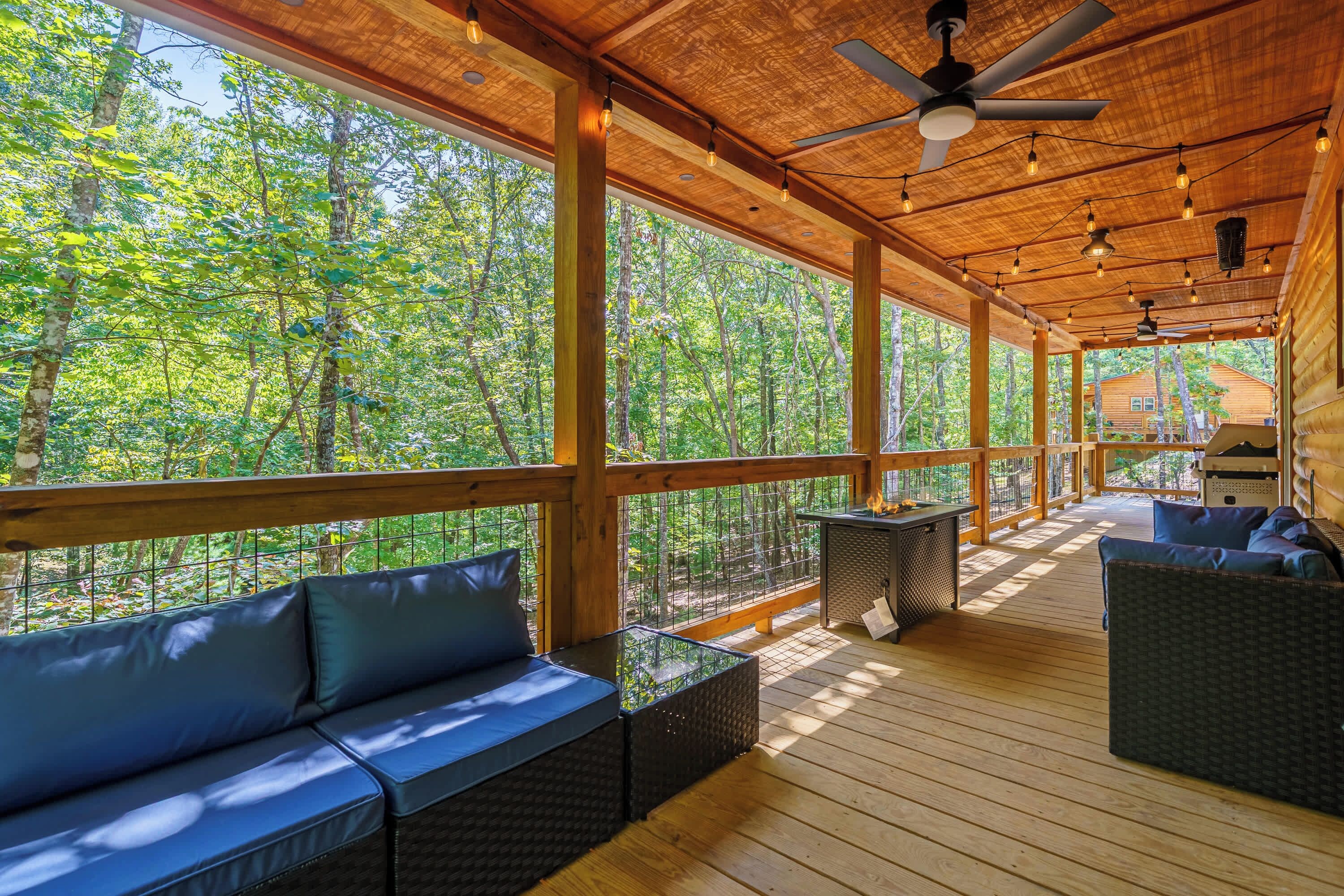 A covered outdoor deck with wooden flooring, a ceiling fan, and a seating area with a sofa and chairs.