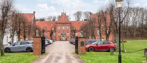 A brick building with a central entrance, surrounded by parked cars and a paved driveway.