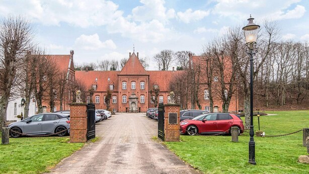 A large brick building with a central entrance, surrounded by parked cars and a grassy area. - 4 Star Holiday Home in Skanderborg (Skanderborg)