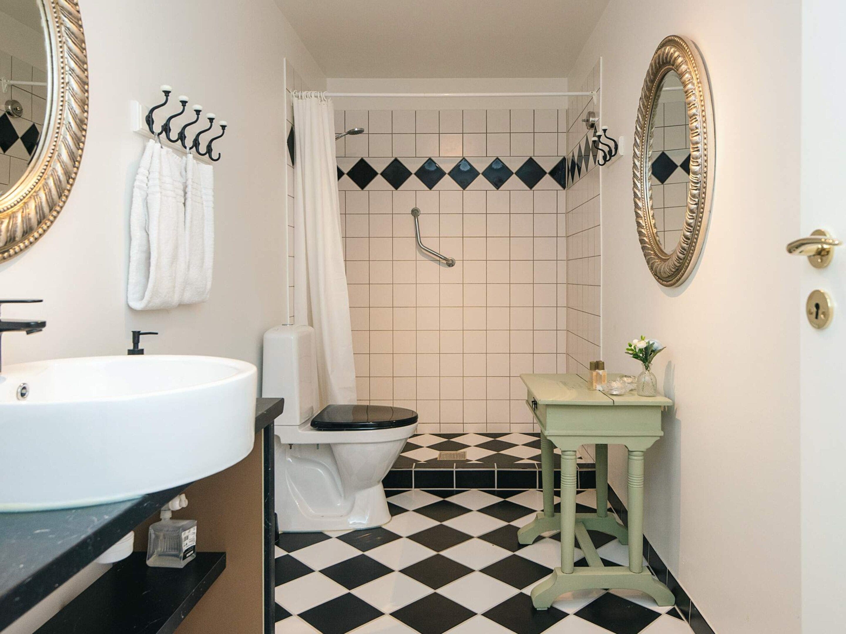 Une salle de bain avec un lavabo blanc, un carrelage noir et blanc, un meuble-lavabo vert et une douche avec un rideau blanc.