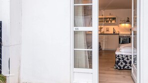 A white exterior wall with a sliding glass door leading to a kitchen with wooden flooring, a stove, and a dining area with a table and chairs. - 4 Star Holiday Home in Skanderborg (Skanderborg)