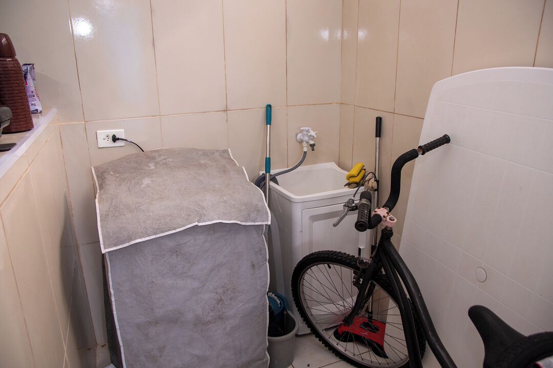 A bathroom with a tiled floor, a small sink, a bicycle, and a covered object.