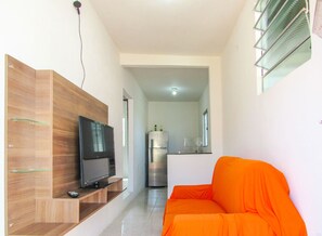 A modern living room with a wooden entertainment unit, a flat-screen TV, and an orange sofa. - Espaço de Lazer: Casa com Piscina e Churrasqueira (Vera Cruz)