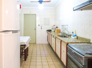 A compact kitchen with a refrigerator, stove, sink, and a dining area with a table and chairs. - Apto a 600 metros da Praia Grande, em Ubatuba/SP (Ubatuba)