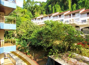 A hotel with multiple floors, surrounded by lush greenery and a small water body. - Apto a 600 metros da Praia Grande, em Ubatuba/SP (Ubatuba)