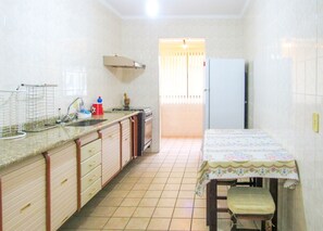 A compact kitchen with a sink, stove, and a table with a floral tablecloth. - Apto a 600 metros da Praia Grande, em Ubatuba/SP (Ubatuba)
