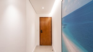 A hallway with a wooden door and a large painting of a beach scene. - Incrível apartamento com Wi-Fi na Praia Brava/SC (Itajaí)