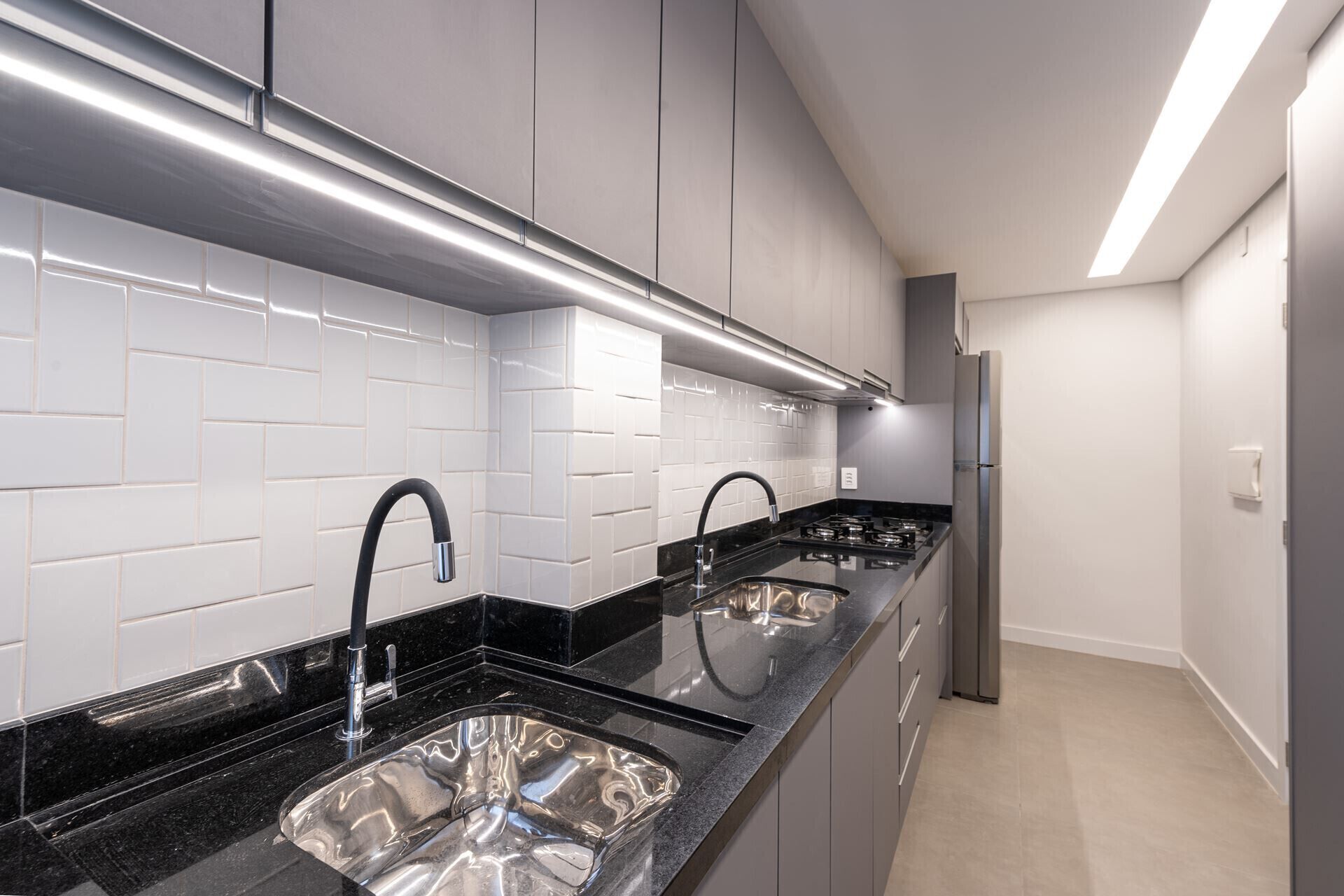 Uma cozinha moderna com azulejos brancos tipo metrô, bancadas pretas, pias de aço inoxidável e forno embutido.