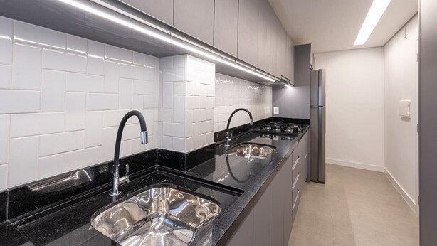 A modern kitchen with white subway tiles, black countertops, stainless steel sinks, and a built-in oven. - Incrível apartamento com Wi-Fi na Praia Brava/SC (Itajaí)