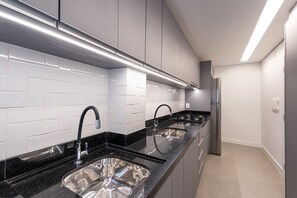 Ett modernt kök med vita, rektangulära kakelplattor, svarta bänkskivor, diskhoar i rostfritt stål och en inbyggd ugn.