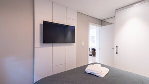 A bedroom with a bed, a flat-screen TV mounted on the wall, and a door leading to another room. - Incrível apartamento com Wi-Fi na Praia Brava/SC (Itajaí)