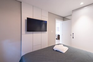 Ein Schlafzimmer mit Bett, einem an der Wand befestigten Flachbildfernseher und einer Tür zu einem weiteren Raum.