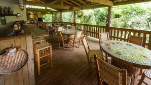 A wooden deck with a bar area, round tables, and wicker chairs.
