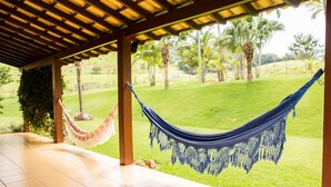 Un hamac sous une pergola en bois, avec vue sur une zone herbeuse et des arbres.