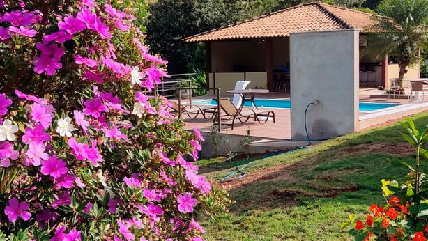 Un espace aménagé au bord de la piscine, avec un petit bâtiment, des sièges extérieurs et une vue sur un paysage vallonné.