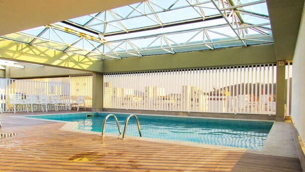 Una piscina interior con plataforma de madera, techo de cristal y barreras blancas.