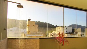 Un balcón con ducha, una planta en maceta y vistas a edificios y colinas.