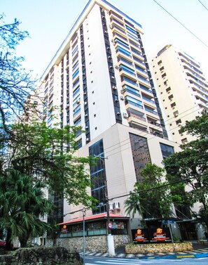 A high-rise building with multiple floors, large windows, and a stone facade. - Apto a 200m Praia Pitangueiras | Piscina e Sauna (Guarujá)