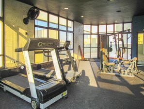 A gym with treadmills, weight machines, and a large windowed wall. - Apto a 200m Praia Pitangueiras | Piscina e Sauna (Guarujá)