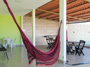 A room with a hammock, white chairs, a table, and a tiled wall. - Casa com Piscina e Área Gourmet | Taipu de Fora (Maraú)