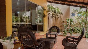 Un patio con mobiliario de mimbre, plantas en macetas y una pared de vidrio.