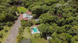 Vista aérea de una zona residencial con piscina, una casa con techo rojo y árboles densos alrededor.