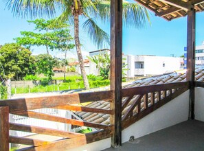 A wooden staircase leading to a covered outdoor area with a view of greenery and buildings in the background. - Casa a 250m da Praia do Sul com Wi-Fi em Ilhéus/BA (Ilhéus)