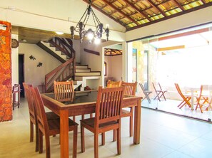 A dining area with a wooden table and chairs, a staircase, and a view of the outside. - Casa a 250m da Praia do Sul com Wi-Fi em Ilhéus/BA (Ilhéus)