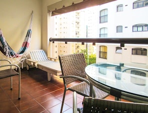 Un balcón con una hamaca, dos sillones de relax, una mesa y vistas a un edificio de gran altura.