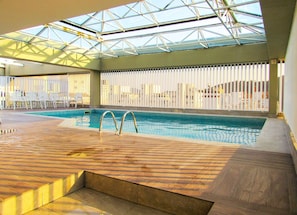 Una piscina interior con plataforma de madera, techo de cristal y barreras blancas.