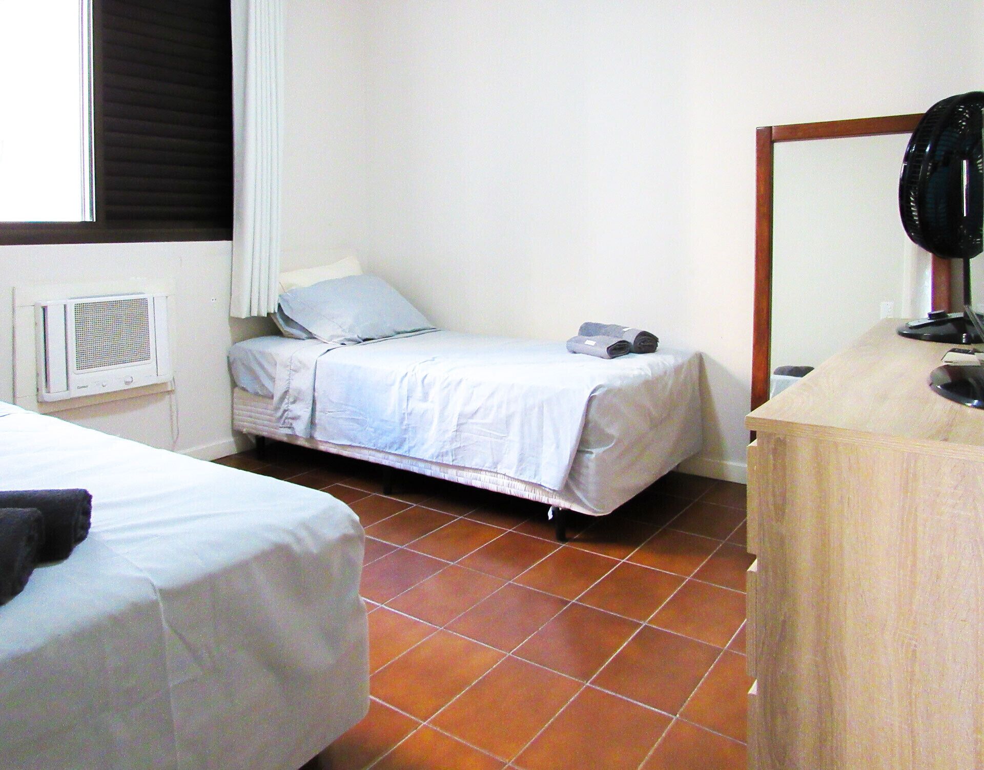 Een kleine, net kamer met twee eenpersoonsbedden, een houten bureau, een spiegel en een radiator.