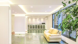 A modern living room with a sofa and a large window. - Apto c/ Piscina e Sauna | 200m Praia Pitangueiras (Guarujá)
