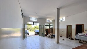 Un'ampia stanza con pavimento piastrellato di bianco, una panca in legno e un letto. Sono presenti due porte, una che dà verso l'esterno e un'altra verso una stanza più piccola.