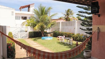 Un hamac dans un jardin, avec une piscine, une clôture blanche et un palmier.