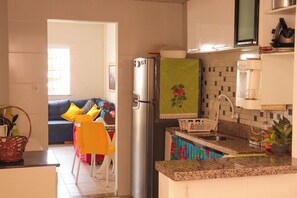 A compact kitchen with a refrigerator, sink, and a small dining area with a chair and table. - Casa de andar a 200m da areia -Praia da Caueira/SE (Itaporanga D'Ajuda)