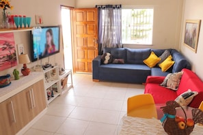 A living room with a blue sofa, red couch, and a television on a white cabinet. - Casa de andar a 200m da areia -Praia da Caueira/SE (Itaporanga D'Ajuda)