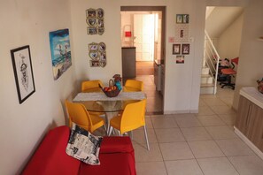 A dining area with a glass table and yellow chairs, a red sofa, and various framed pictures on the walls. - Casa de andar a 200m da areia -Praia da Caueira/SE (Itaporanga D'Ajuda)
