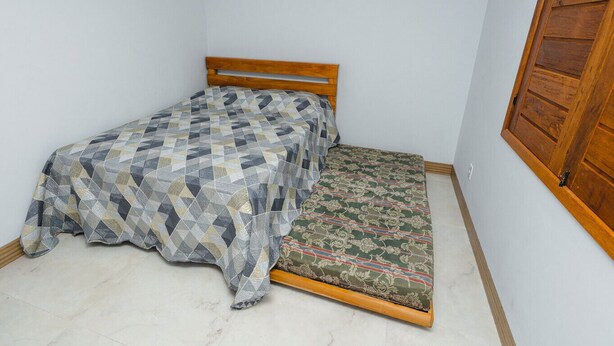 Een kleine kamer met een enkel bed, een houten hoofdbord en een bedovertrek met dessin.