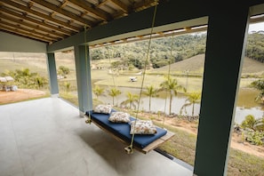 A room with a swing bed overlooking a water body and a hilly landscape. - Linda casa de campo com Wi-Fi em Santa Teresa/ES (Santa Teresa)