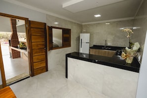 A modern kitchen with a black countertop, a white refrigerator, and a wooden door. - Linda casa de campo com Wi-Fi em Santa Teresa/ES (Santa Teresa)