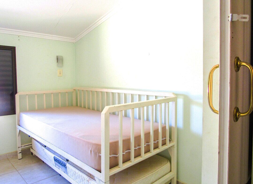 Une petite chambre avec un lit simple, un cadre de lit blanc, une porte avec une poignée en laiton et un interrupteur sur le mur.
