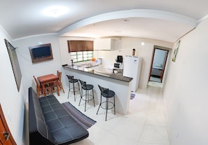 Uma cozinha compacta com geladeira embutida, micro-ondas e cafeteira. Há uma área de refeições com um sofá e dois banquetas.