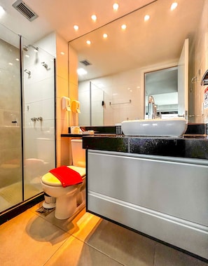 Ein modernes Badezimmer mit Duschkabine aus Glas, Toilette mit rotem Deckel, weißem Waschbecken und großem Spiegel darüber.