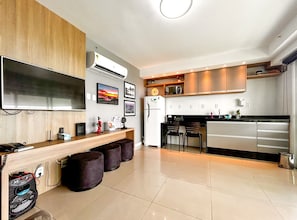 A modern kitchen with a flat-screen TV, built-in oven, and a dining area with stools. - Studio com Varanda e Piscina| Beira Mar no Recreio (Rio de Janeiro)