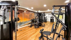 Una palestra con diverse macchine per esercizi, un pavimento in legno e un'ampia finestra vista mare.