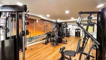 A gym with various exercise machines, a wooden floor, and a large window with a view of the ocean.