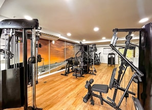Ein Fitnessstudio mit verschiedenen Trainingsgeräten, einem Holzboden und einem großen Fenster mit Meerblick.