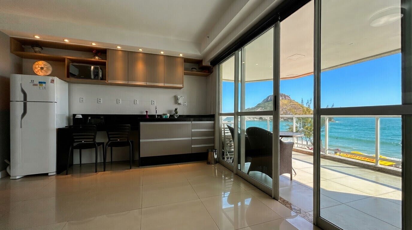 Uma cozinha moderna com geladeira, micro-ondas e fogão, que dá para uma varanda com vista para o mar.